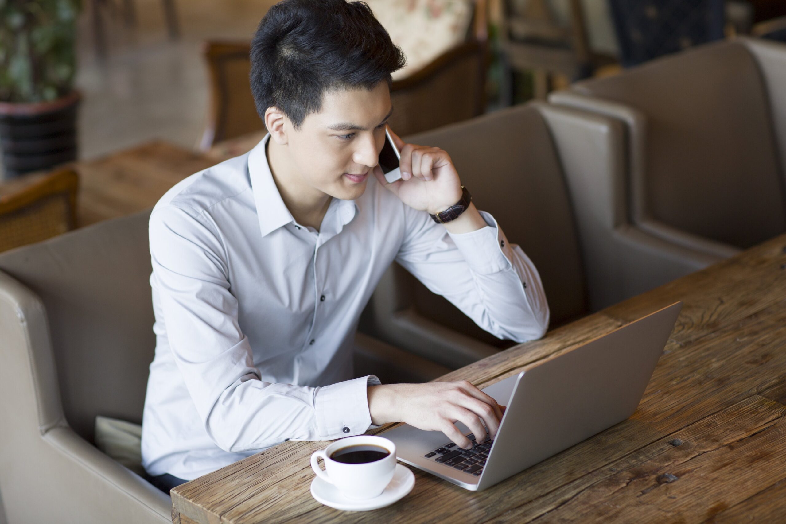 young-man-talking-on-phone-and-using-laptop-in-caf-2022-03-25-00-29-01-utc (1)